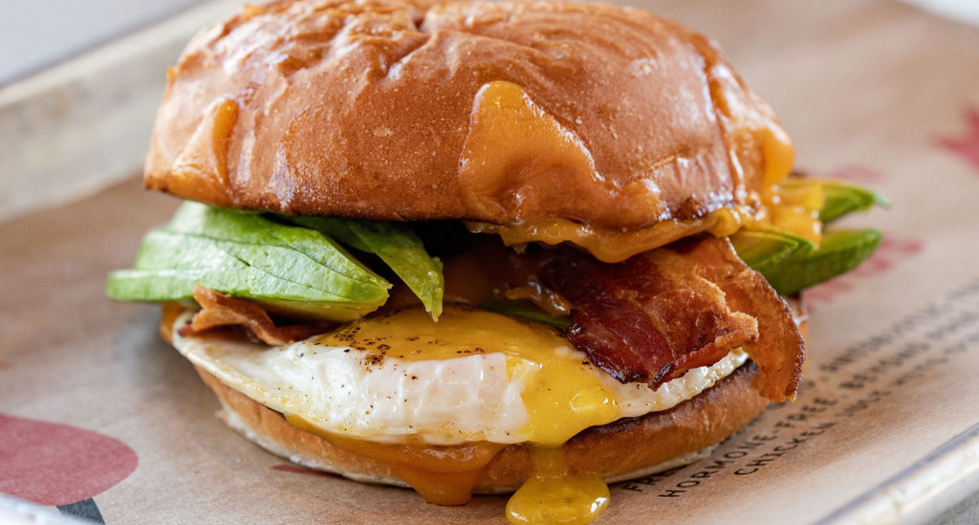 Image of a sandwich with a dripping egg, bacon, avocado, and cheese on a tray