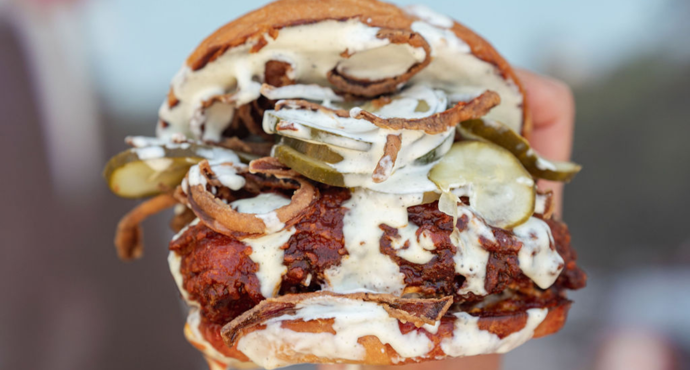 Image of a spicy sandwich with pickles, fried onions, and ranch.